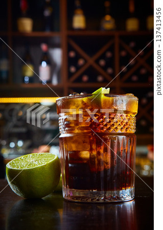 Dark amber cocktail in a tactile crystal glass, featuring fresh lime accents 137413456