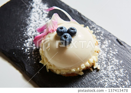 Elegant white chocolate mousse dome dessert topped with fresh blueberries and a floral petal 137413478