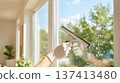 Hand using squeegee to clean window glass in bright room. Natural light filters through the window. Concept of cleaning services, home improvement, window care. 137413480