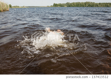child happily excitedly enters water, swims, dives lake or pond on a hot, sunny summer day during vacation or school break. active healthy lifestyle. child wearing turquoise swimming trunks goggles. child happily excitedly enters water, swims, dives lake or pond on a hot, sunny summer day during vacation or school break. active healthy lifestyle. child wearing turquoise swimming trunks goggles. 137413512