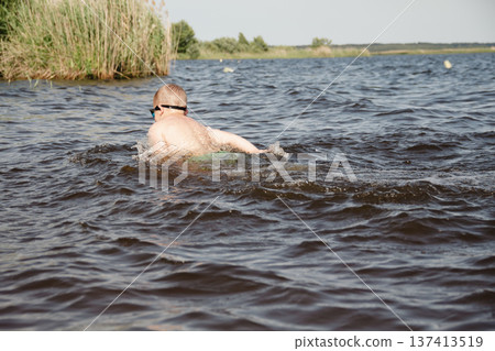 child happily excitedly enters water, swims, dives lake or pond on a hot, sunny summer day during vacation or school break. active healthy lifestyle. child wearing turquoise swimming trunks goggles. child happily excitedly enters water, swims, dives lake or pond on a hot, sunny summer day during vacation or school break. active healthy lifestyle. child wearing turquoise swimming trunks goggles. 137413519