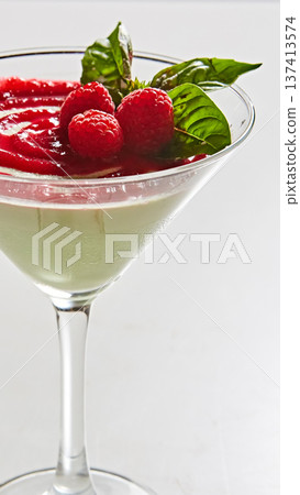 Gourmet panna cotta served in a martini glass with a vibrant raspberry coulis swirl and fresh mint 137413574