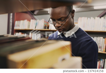 University, student and black man in a library reading and learning on campus for knowledge and education in college. Smart, clever and person doing research with books on a shelf for an exam 137414158