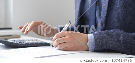 Professional accountant calculating expenses, documenting financial details on notepad while working at corporate desk. Audit and taxes in business 137414786