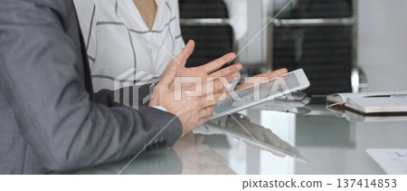 Business professionals collaborating at a meeting, discussing financial data on a digital tablet in modern office. Business-people concept Business professionals collaborating at a meeting, discussing financial data on a digital tablet in modern office. Business-people concept 137414853