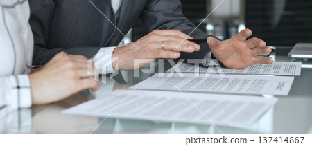 Business executive hands gesturing over contract on glass table during formal office meeting negotiating legal agreement terms. Business people concept Business executive hands gesturing over contract on glass table during formal office meeting negotiating legal agreement terms. Business people concept 137414867