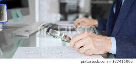 Hand holding magnifying glass, inspecting financial document, performing audit and business analysis. Audit and taxes in business 137415002