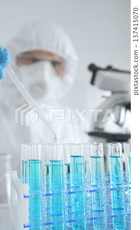 Scientific researcher wearing protective equipment, carefully pipetting liquid into test tubes while conducting medical research experiment. Medicine, healthcare and science concept Scientific researcher wearing protective equipment, carefully pipetting liquid into test tubes while conducting medical research experiment. Medicine, healthcare and science concept 137415070