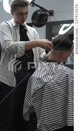 Professional barber carefully trimming customer's hair with electric clipper, providing a stylish and precise haircut in a modern barbershop environment 137415074