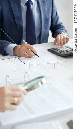 Professional male accountant calculating taxes and analyzing financial data in office setting. Audit and taxes in business Professional male accountant calculating taxes and analyzing financial data in office setting. Audit and taxes in business 137415099
