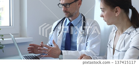 Male doctor showing medical test results on a laptop to a female patient, discussing diagnosis and treatment options in a bright medical office. Medicine and health care Male doctor showing medical test results on a laptop to a female patient, discussing diagnosis and treatment options in a bright medical office. Medicine and health care 137415117