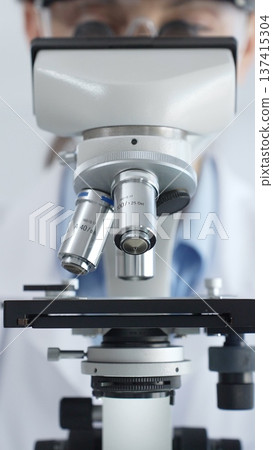 Scientist wearing lab coat and protective glasses using a modern microscope in a laboratory setting, conducting research and experiments in a scientific environment. Health care and science concept Scientist wearing lab coat and protective glasses using a modern microscope in a laboratory setting, conducting research and experiments in a scientific environment. Health care and science concept 137415304