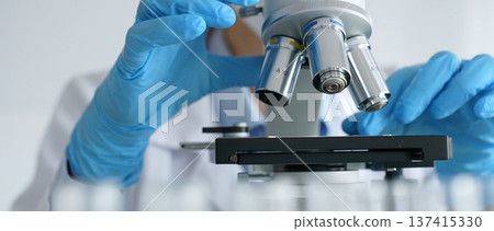 Laboratory scientist wearing blue protective gloves carefully positioning microscope slide, demonstrating research precision. Medicine, healthcare and science concept 137415330
