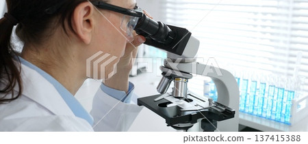 Female scientist examining microscope slide, analyzing research data in sterile laboratory surrounded by scientific glassware and equipment. Medicine, healthcare and science concept Female scientist examining microscope slide, analyzing research data in sterile laboratory surrounded by scientific glassware and equipment. Medicine, healthcare and science concept 137415388
