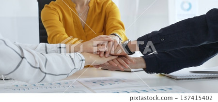 Business professionals joining hands over workplace documents, symbolizing collaborative spirit and shared workplace success Business professionals joining hands over workplace documents, symbolizing collaborative spirit and shared workplace success 137415402