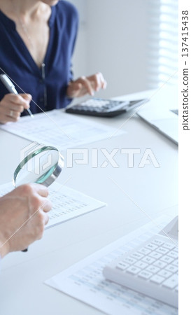 Two professional accountants analyzing financial reports with magnifying glass and calculator, performing accounting and auditing tasks in the office, close up of hands. Audit and taxes in business 137415438