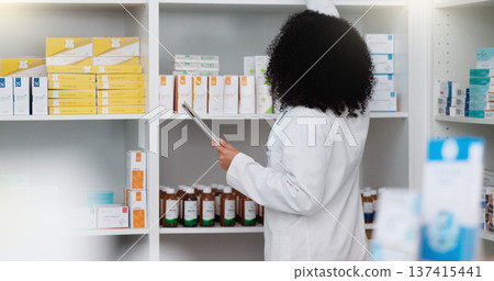 Young and focused pharmacist use her tablet to do stock taking in a modern pharmacy drugstore. Multiethnic female health professional worker or medication expert in a chemist using a digital gadget 137415441