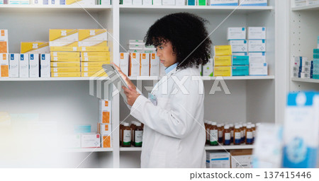 Young and focused pharmacist use her tablet to do stock taking in a modern pharmacy drugstore. Multiethnic female health professional worker or medication expert in a chemist using a digital gadget 137415446