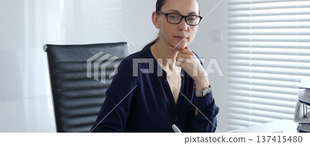 Businesswoman signing and reviewing accounting documents while calculating financial data in a corporate office setting. Audit and taxes in business Businesswoman signing and reviewing accounting documents while calculating financial data in a corporate office setting. Audit and taxes in business 137415480
