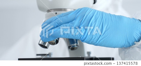 Close up of virologist's hands in blue gloves adjusting microscope in laboratory, conducting scientific research and analysis. Health care, medicine and science concept 137415578
