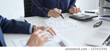 Business team analyzing financial documents, using calculators and laptop, working together on project in modern office. Audit and taxes concept Business team analyzing financial documents, using calculators and laptop, working together on project in modern office. Audit and taxes concept 137415591