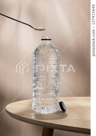 A spoon pouring pink salt into a clear water bottle on a wooden table to create mineral water. 137415648