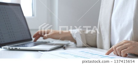 Professional female analyzing financial reports, reviewing charts on laptop and paper documents while seating at the desk in office. Business people Professional female analyzing financial reports, reviewing charts on laptop and paper documents while seating at the desk in office. Business people 137415654