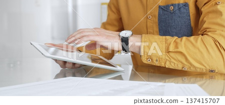 Person using a digital tablet for business at desk, navigating online content or browsing documents. Audit and taxes in business Person using a digital tablet for business at desk, navigating online content or browsing documents. Audit and taxes in business 137415707