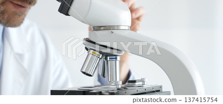 Close up of an adult male scientist carefully using a microscope, examining a sample in a laboratory setting, conducting important research. Medicine and science concept Close up of an adult male scientist carefully using a microscope, examining a sample in a laboratory setting, conducting important research. Medicine and science concept 137415754