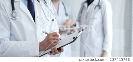 During a discussion with the medical team, a physician takes notes on a clipboard, capturing aspects of collaborative patient care, documentation, and clinical healthcare strategies 137415788