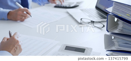 Auditors collaborating in modern office, analyzing financial documents and using calculator with a laptop displaying charts. Audit and taxes in business Auditors collaborating in modern office, analyzing financial documents and using calculator with a laptop displaying charts. Audit and taxes in business 137415799