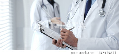 Doctor taking notes on clipboard during discussion with medical team involved in collaborative patient care, documentation, and health care strategy development in clinic 137415811
