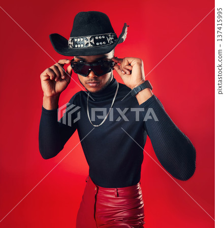 Fashion, man and cowboy hat, sunglasses and trendy clothes with gen z isolated on red background. Confident model, cool and leather pants with eyewear accessory, western aesthetic and edgy in studio Fashion, man and cowboy hat, sunglasses and trendy clothes with gen z isolated on red background. Confident model, cool and leather pants with eyewear accessory, western aesthetic and edgy in studio 137415995
