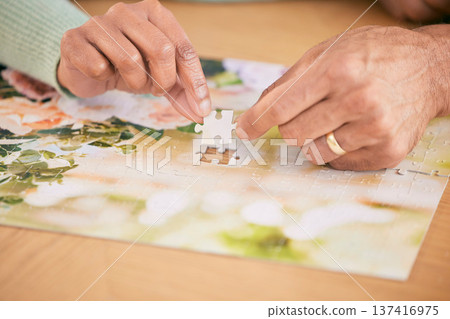 Puzzle on table, piece and hands of couple in home for bonding, fun activity and relax together. Retirement, marriage and closeup of people with jigsaw for playing games, hobby and entertainment Puzzle on table, piece and hands of couple in home for bonding, fun activity and relax together. Retirement, marriage and closeup of people with jigsaw for playing games, hobby and entertainment 137416975