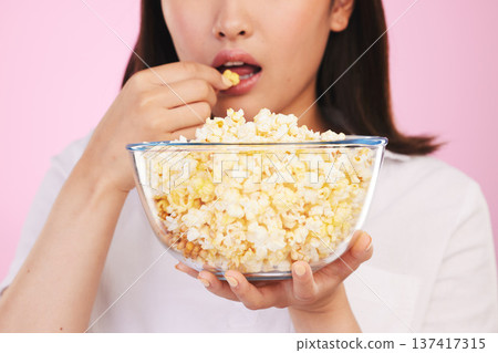 Popcorn, hungry and woman hands eating a movie snack in a studio with watching tv and food. Pink background, female person and mouth with chips in a glass bowl with film and series subscription Popcorn, hungry and woman hands eating a movie snack in a studio with watching tv and food. Pink background, female person and mouth with chips in a glass bowl with film and series subscription 137417315