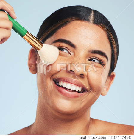Face, happy woman and brush for makeup in studio to apply foundation for glow on blue background. Model, smile and aesthetic cosmetics for skincare tools, facial beauty powder or thinking of makeover 137417498