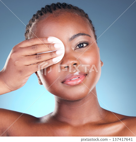 Portrait, beauty and cotton swab with a black woman in studio on a blue background for skincare. Face, hygiene and cosmetics with a young model cleaning her skin for wellness or antiaging care Portrait, beauty and cotton swab with a black woman in studio on a blue background for skincare. Face, hygiene and cosmetics with a young model cleaning her skin for wellness or antiaging care 137417641