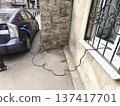 Charging a car outside through a window on the ground floor of a building. Some countries offer a 50% discount on electricity bills for apartments 137417701