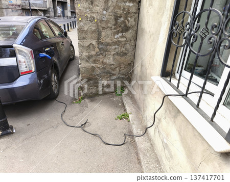 Charging a car outside through a window on the ground floor of a building. Some countries offer a 50% discount on electricity bills for apartments 137417701