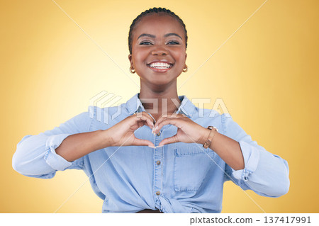 Happy black woman, portrait and heart hands for support, love or care against a yellow studio background. Face of African female person smile with loving emoji, shape or symbol icon on valentines day 137417991