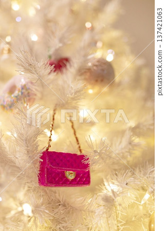 A vibrant pink handbag ornament hanging on a white Christmas tree with warm glowing lights. A chic, playful holiday close-up perfect for festive designs and stylish seasonal themes. A vibrant pink handbag ornament hanging on a white Christmas tree with warm glowing lights. A chic, playful holiday close-up perfect for festive designs and stylish seasonal themes. 137421063