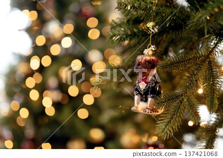 A charming Christmas tree ornament shaped like a dressed-up dog, surrounded by warm golden bokeh lights. A festive and whimsical holiday scene perfect for seasonal designs. A charming Christmas tree ornament shaped like a dressed-up dog, surrounded by warm golden bokeh lights. A festive and whimsical holiday scene perfect for seasonal designs. 137421068