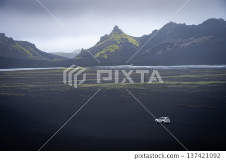 Offroad vehicle passing through black volcanic landscape with mountains in back, Highlands Iceland Offroad vehicle passing through black volcanic landscape with mountains in back, Highlands Iceland 137421092