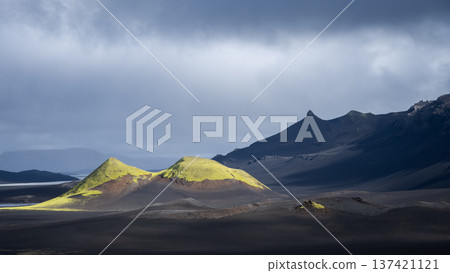 Black volcanic landscape with cloudy sky and two green illuminated mountains , Highlands Iceland Black volcanic landscape with cloudy sky and two green illuminated mountains , Highlands Iceland 137421121