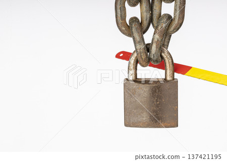 A Close-Up of a Weathered Metal locked Padlock with a Rusty Chain and a Brightly Colored Hacksaw Attempting to Cut Through in a Dramatic Display of Security Challenge 137421195