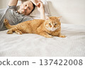 Man lying on white bed with his ginger cat 137422008