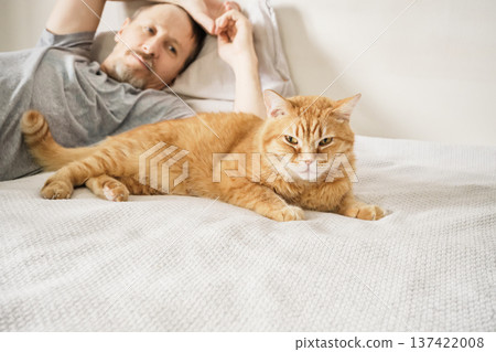 Man lying on white bed with his ginger cat 137422008