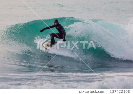 Surfer rides hollow turquoise barrel wave in cold ocean water, surfing action Surfer rides hollow turquoise barrel wave in cold ocean water, surfing action 137422108