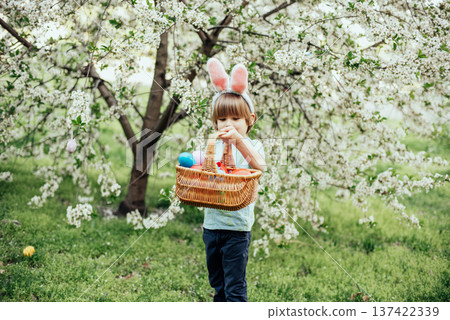 Easter egg hunt. child Wearing Bunny Ears Running To Pick Up Egg In Garden. Easter tradition. Baby with basket full of colorful eggs. Easter egg hunt. child Wearing Bunny Ears Running To Pick Up Egg In Garden. Easter tradition. Baby with basket full of colorful eggs. 137422339