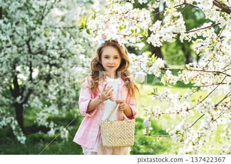 Outdoor Easter celebration, childhood joy and seasonal tradition. Little girl with bunny ears holding decorative Easter egg and wicker basket under blooming spring tree. Outdoor Easter celebration, childhood joy and seasonal tradition. Little girl with bunny ears holding decorative Easter egg and wicker basket under blooming spring tree. 137422367